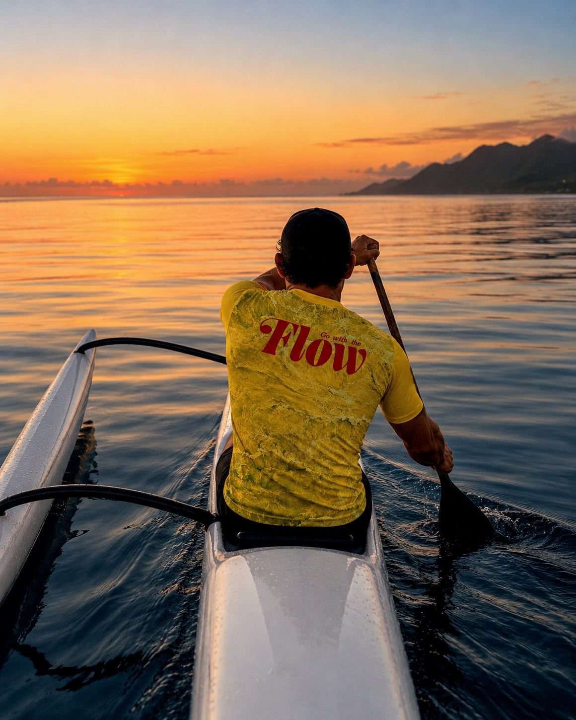 A paddler in the yellow Nalu jersey, seen from behind, in an OC1 at dawn