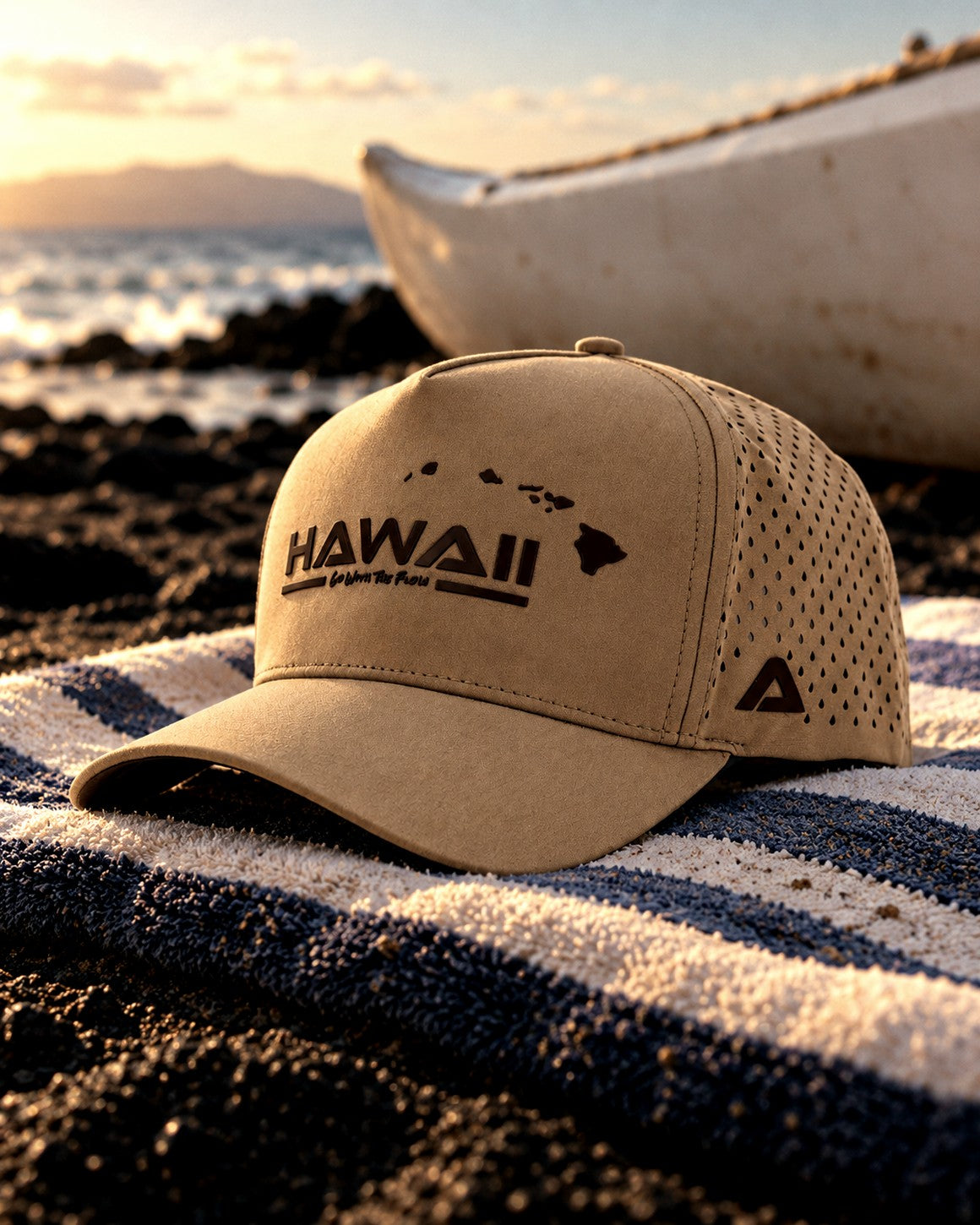 The khaki Hawaiʻi snapback on a beach towel beside a canoe hull