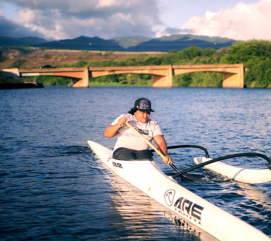 A paddler in a white OC1 on calm water near a bridge