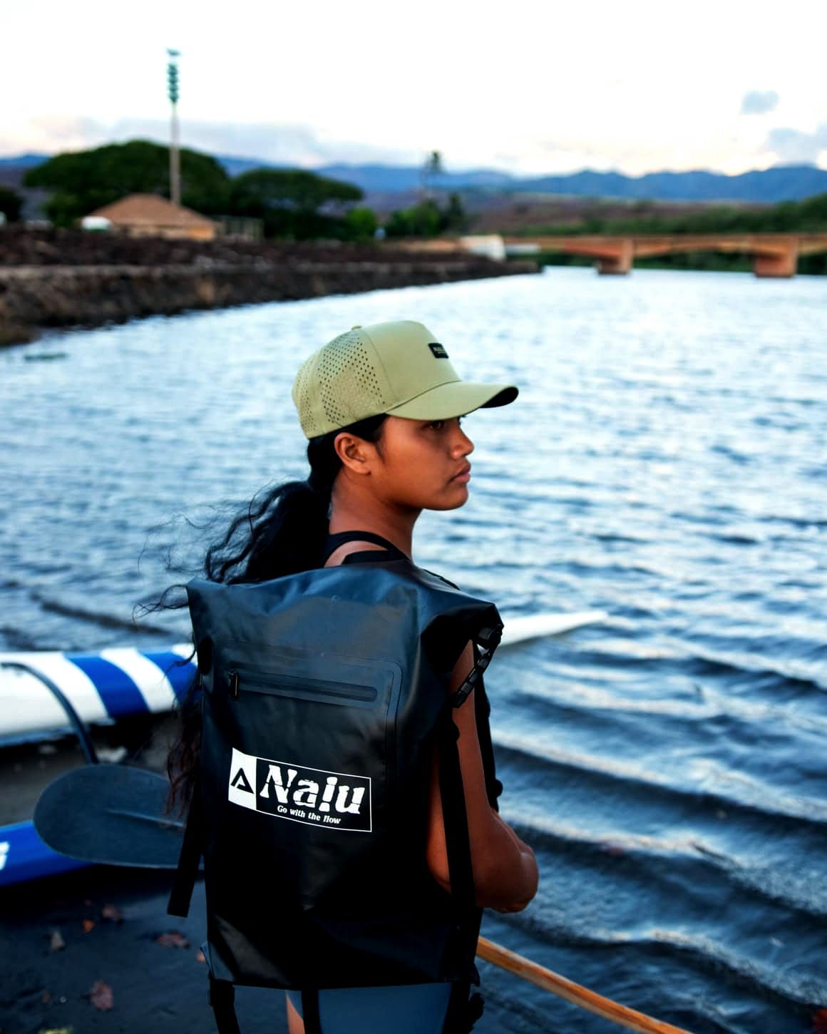 A paddler wears the black Nalu dry bag backpack at the water's edge