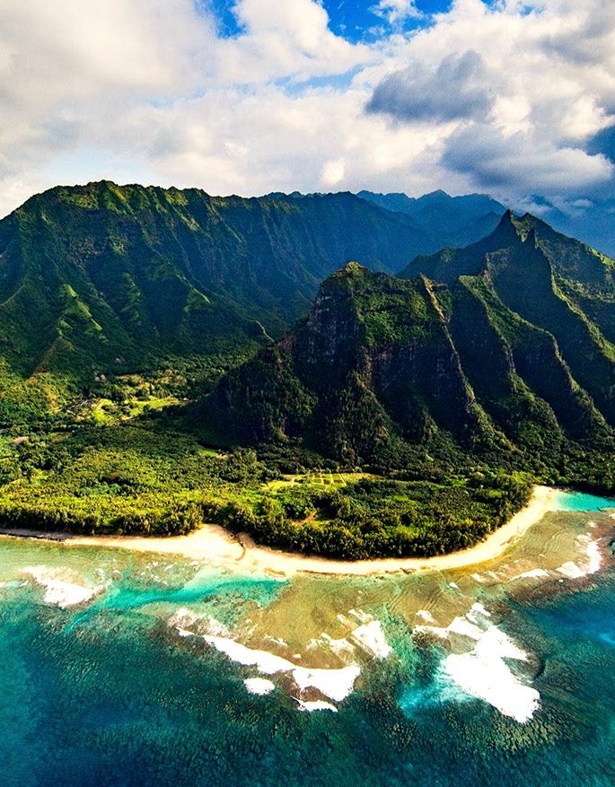 Aerial view of the Nā Pali coast, its green ridges falling to a reef-lined beach