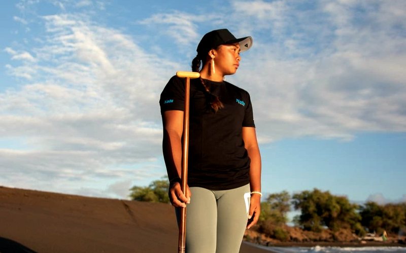 A paddler holds her paddle on a dark-sand beach