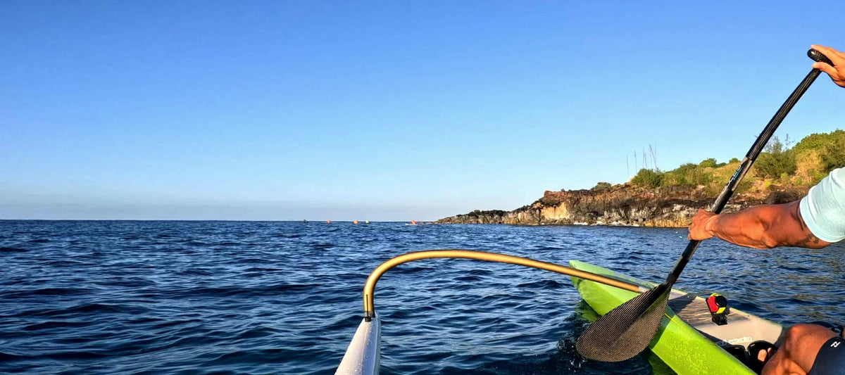 Open water seen from an outrigger canoe, its ama on the left and a paddler's arm at the edge