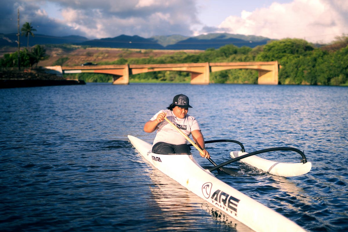 A paddler in a white OC1 on calm water near a bridge