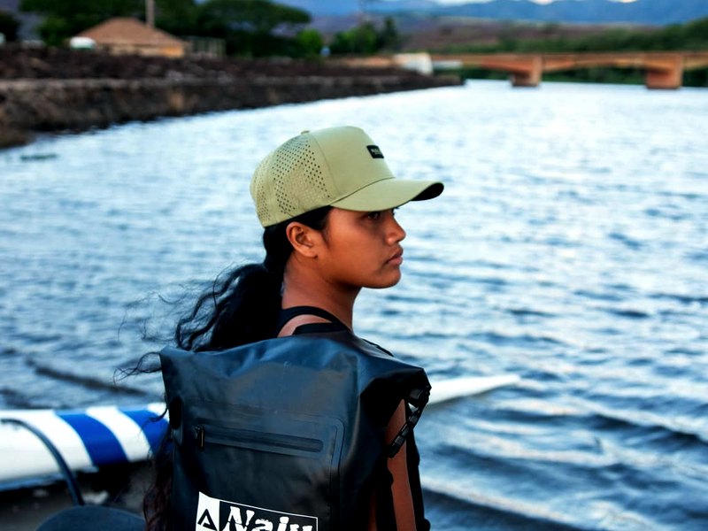 A paddler wears the black Nalu dry bag backpack at the water's edge