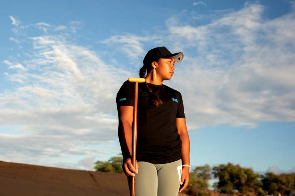 A paddler stands with her paddle on a dark-sand beach