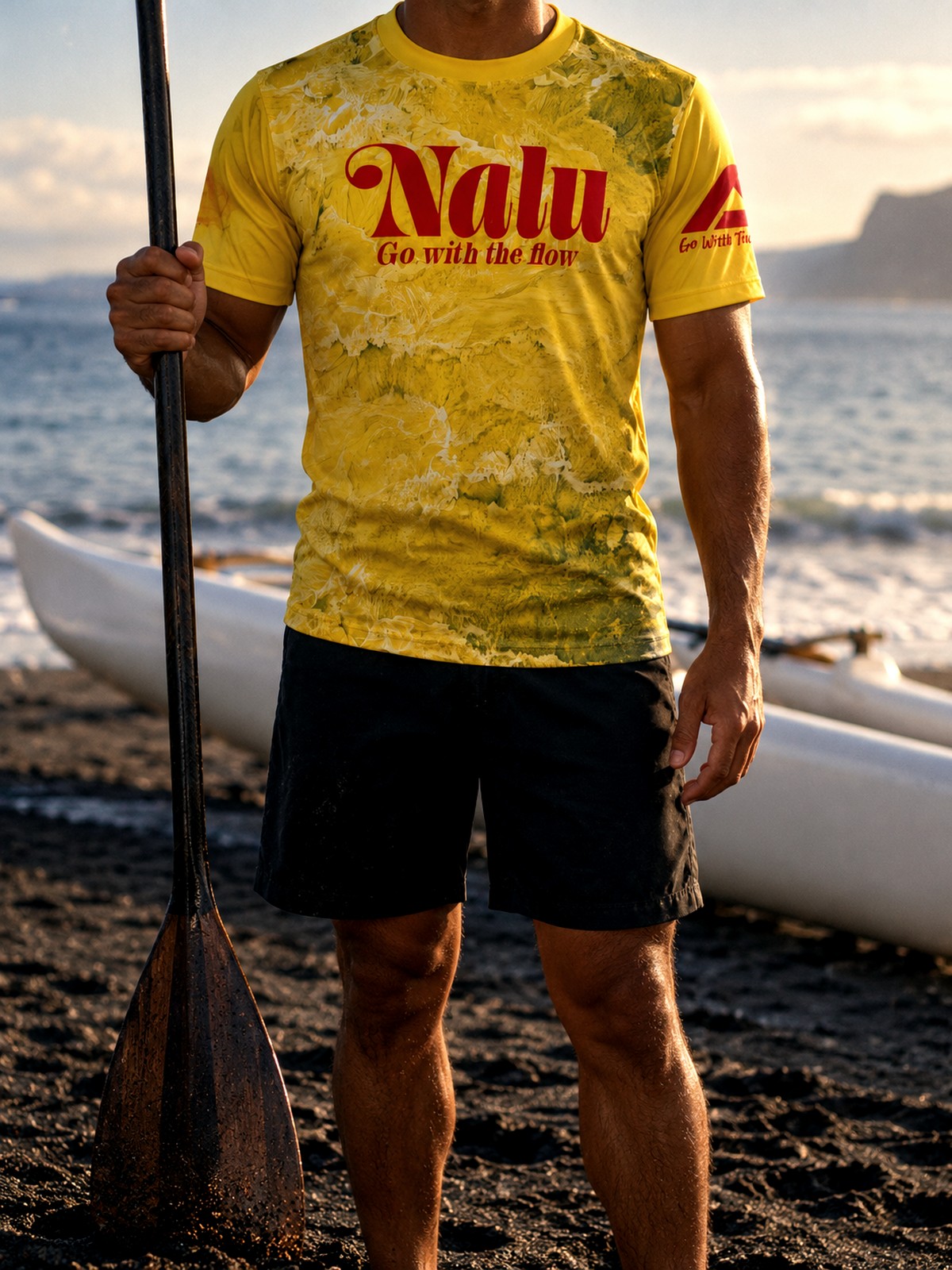 A paddler in the yellow Nalu jersey holding a paddle at the water's edge